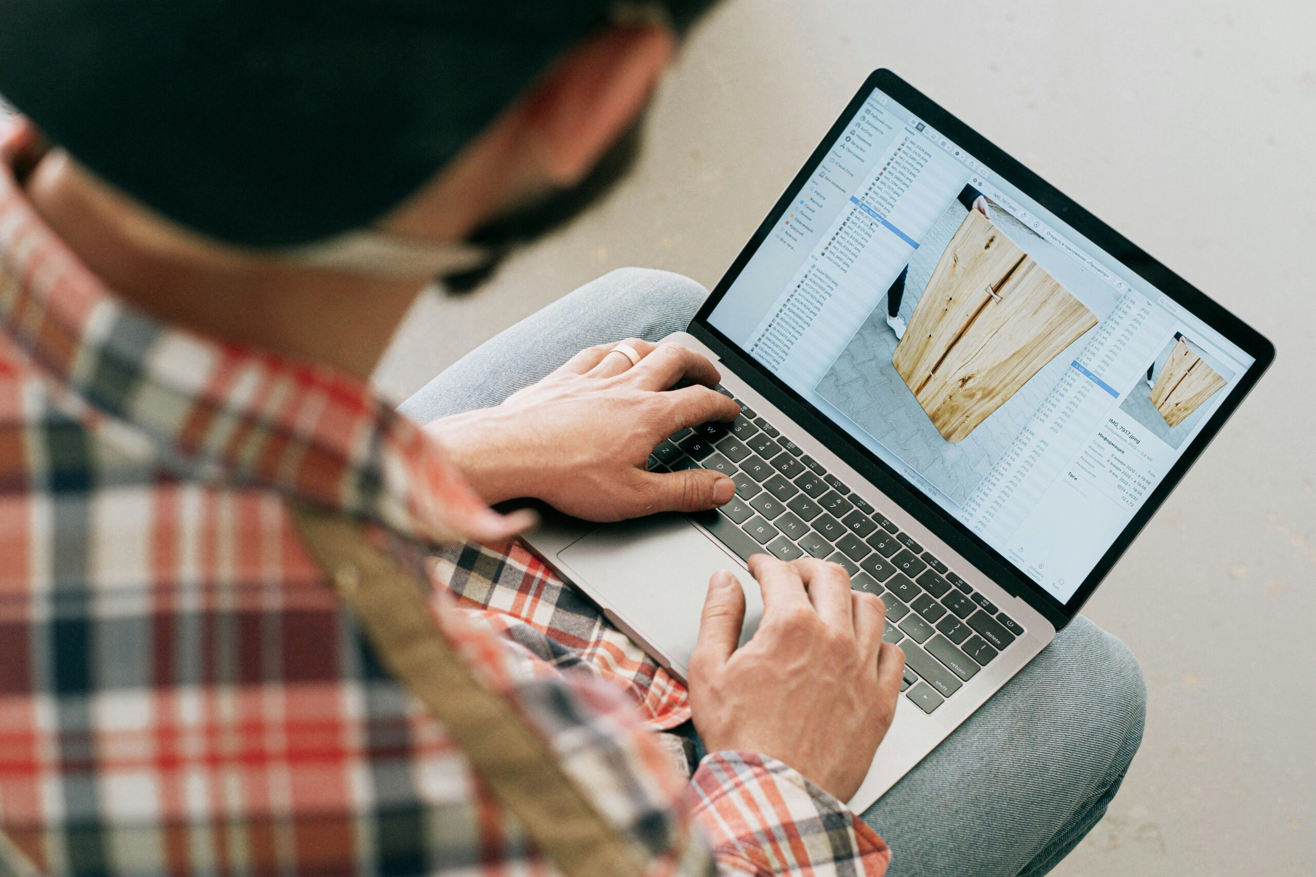 A craftsman uses a laptop to design wooden furniture in a workshop setting.